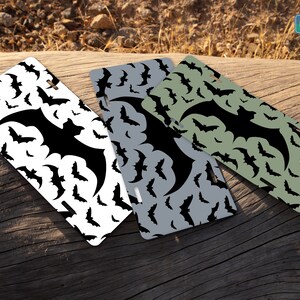 May include: Three different license plates with a black bat silhouette on a white, gray, and green background. The plates have a repeating pattern of bats. The text "CAR BAR" is on a green rectangle in the top right corner of the image.