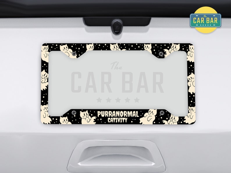 Puede incluir: Marco de matr&iacute;cula negro y blanco con un patr&oacute;n repetitivo de gatos blancos. El marco tiene el texto "The Car Bar" y "Purranormal Cattivity" impreso en &eacute;l.