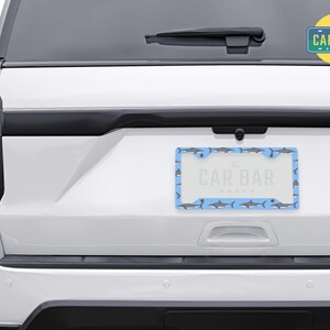 May include: A white car with a blue and gray shark patterned license plate frame that says "The Car Bar".