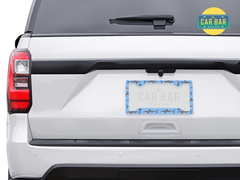 May include: A white car with a blue and gray shark patterned license plate frame that says "The Car Bar".