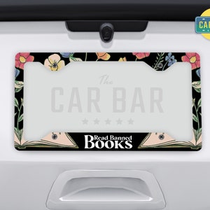 May include: A black license plate frame with a floral design and the text "The Car Bar" and "Read Banned Books".