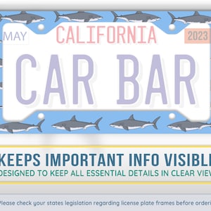 May include: A blue license plate frame with a shark pattern. The frame has a white background with the text "MAY", "CALIFORNIA", "2023", "CAR BAR" and "KEEPS IMPORTANT INFO VISIBLE". The text "DESIGNED TO KEEP ALL ESSENTIAL DETAILS IN CLEAR VIEW" is also included.