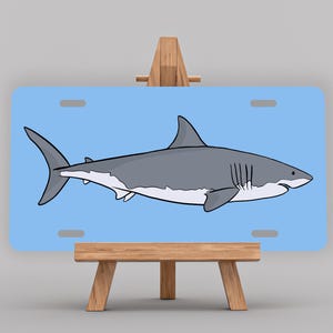 May include: A blue and white great white shark illustration on a light blue background. The image is displayed on a wooden easel.
