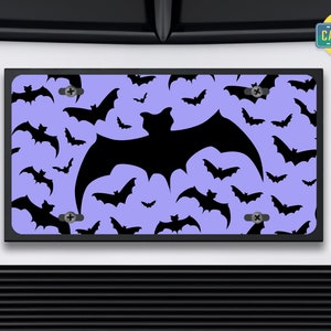 May include: A purple license plate with a black bat silhouette pattern. The bat silhouette is repeated throughout the plate. The plate has two screw holes on the top and bottom. The text "The Car Bar" is visible in the upper right corner of the image.