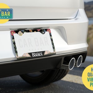May include: A black and white license plate frame with a floral design and the text "The Car Bar" and "Read Beyond Books".
