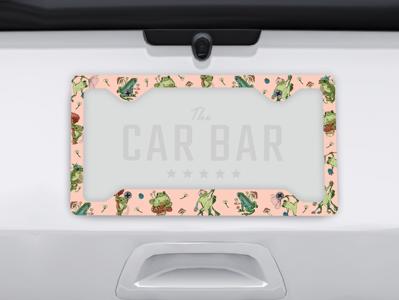 May include: A pink and green license plate frame with a frog pattern and the text "The Car Bar" in the centre.