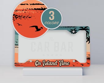 May include: A rectangular license plate frame featuring a sunset beach scene with silhouettes of palm trees and birds. The text "On Island Time" is printed in black at the bottom. A circular overlay displays "3 COLORS" in white text on a teal background.