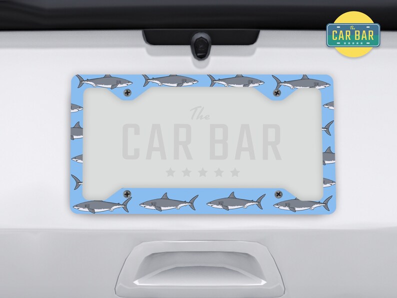 May include: A blue license plate frame with a white shark pattern and the text "The Car Bar" in white.