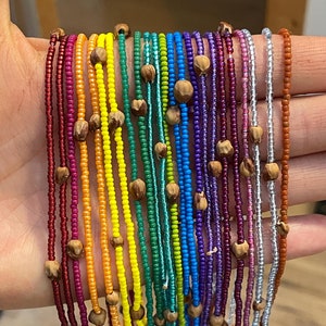 Może przedstawiać: Kolekcja kolorowych naszyjników z koralików z drewnianymi koralikami. Naszyjniki są ułożone w tęczę, a każdy kolor reprezentuje inny odcień.