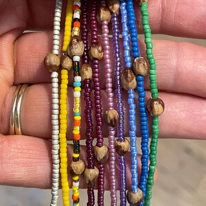 May include: A set of ten beaded bracelets with different colored beads and wooden accents. The bracelets are arranged in a row, with the beads facing the viewer.