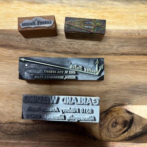 Pode incluir: Quatro blocos de impressão de madeira vintage. O primeiro bloco é marrom e diz "CARPET VALUES". O segundo bloco é de cobre e tem um design geométrico. O terceiro bloco é preto e diz "EDINA, MINNESOTA 55435  6001 W 77th STREET  Sector Sales". O quarto bloco é preto e diz "MINNEAPOLIS, MINNESOTA 55423  8319 Pillsbury Avenue South  GARLAND WEDDING".