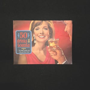 May include: A retro magazine cover with a woman in a pink dress and a man, both holding drinks. The cover displays the text "50 Drinks & Toasts" and the tagline "...to help make you the perfect host."