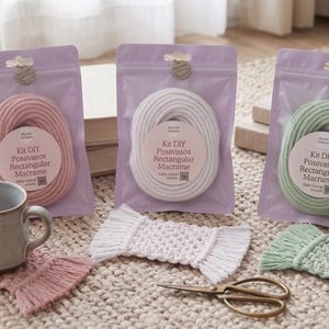 Puede incluir: Kits de posavasos de macramé DIY en rosa, blanco y verde, cada uno empaquetado en una bolsa lavanda. También se ven una taza de cerámica y posavasos terminados, junto con unas tijeras. Los kits incluyen materiales para hacer posavasos de macramé rectangulares.