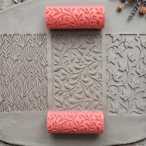 Puede incluir: Una colección de rodillos de textura de arcilla y losas de arcilla texturizadas. Los rodillos son de color coral y rosa, con diseños florales. Las losas de arcilla tienen diseños de hojas y flores. Herramientas para cerámica y artesanía.