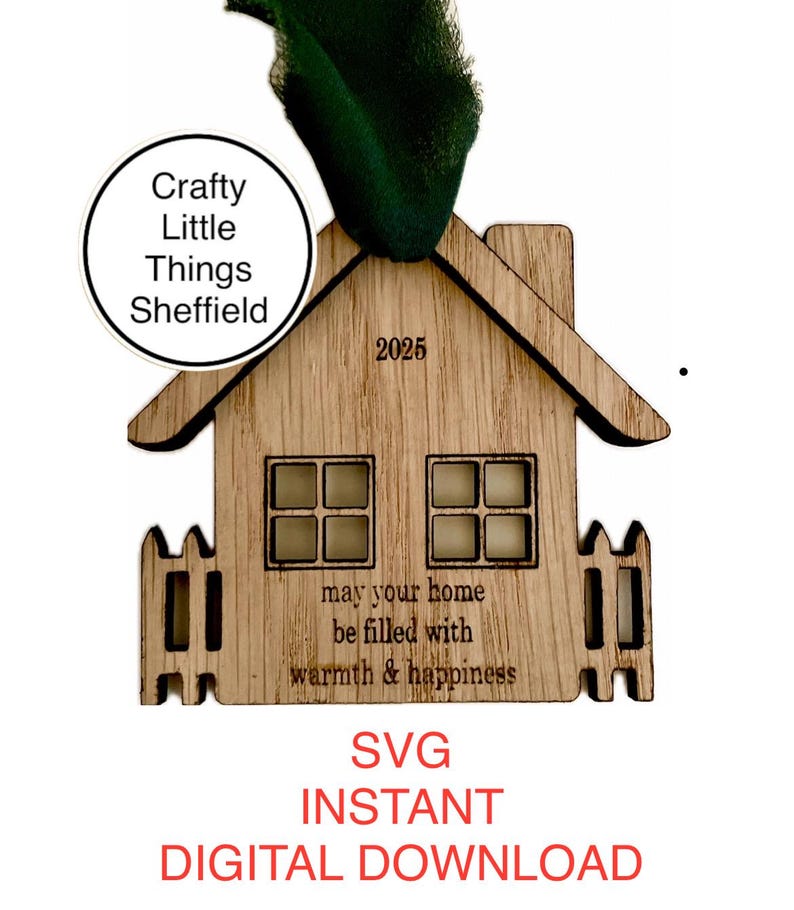 May include: A wooden house ornament with a white picket fence, windows, and the text "may your home be filled with warmth & happiness". The ornament is labelled "Crafty Little Things Sheffield" and "2025".
