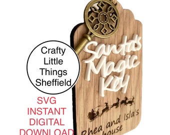 May include: A wooden ornament shaped like a key with the words "Santa's Magic Key" in white lettering. The ornament is decorated with a gold-colored key and a snowflake design. The text "Rhea and Isla's house" is written on the bottom of the ornament.