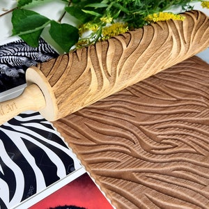 Puede incluir: Rodillo de madera con diseño de estampado de cebra. El rodillo está grabado con el texto "Carla Wood Art".