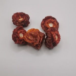 May include: Five dried red peppers with a wrinkled texture and a white centre. The peppers are arranged in a cluster on a white surface.
