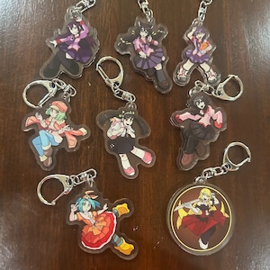 Könnte beinhalten: Ein Set mit acht Schlüsselanhängern mit Anime-Charakteren. Die Schlüsselanhänger sind aus klarem Acryl und zeigen farbenfrohe Illustrationen der Charaktere. Die Schlüsselanhänger sind an silbernen Metallringen befestigt.