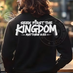 May include: Black sweatshirt with the text "SEEK FIRST THE KINGDOM - MATTHEW 6:33" in white, 3D-style lettering. The sweatshirt has a small crown above the word "KINGDOM". The image also includes a "ORIGINAL" stamp and a "MADE WITH LOVE" stamp.