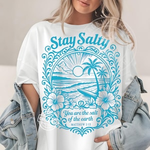 Könnte beinhalten: Weißes T-Shirt mit einem türkisfarbenen Aufdruck. Der Aufdruck zeigt die Worte "Stay Salty" über einer Strandszene mit Palmen und dem Text "You are the salt of the earth" und "Matthew 5:13".