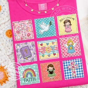 Könnte beinhalten: Ein leuchtend pinkfarbenes T-Shirt mit mehreren quadratischen Aufnähern mit religiösen Symbolen und Phrasen. Zu den Aufnähern gehören ein Kreuz, eine Taube, ein Engel, ein Regenbogen mit "FAITH" und der Satz "JESUS LOVES ME". Das Shirt hat ein Comfort Colors-Etikett.