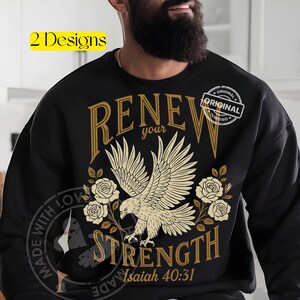 Könnte beinhalten: Schwarzes Sweatshirt mit einem goldenen Adler-Design und den Worten "RENEW your STRENGTH Isaiah 40:31". Das Design beinhaltet Rosen und das Wort "ORIGINAL" in einem Kreis. Der Text "2 Designs" befindet sich in einem gelben Rechteck.