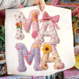 May include: A fabric sign spelling "MAMA" in patchwork letters. The letters feature floral patterns, sunflowers, and a pink bow. The sign is held up by a person.