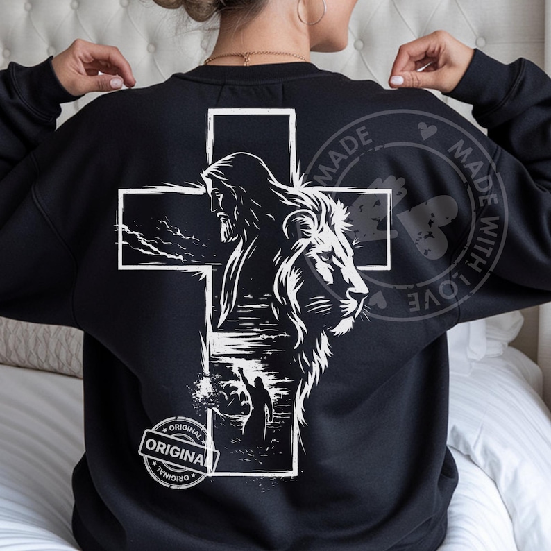 May include: Black sweatshirt featuring a white cross design with a depiction of Jesus and a lion. The design includes the words "ORIGINAL" and "MADE WITH LOVE" in a circular stamp.