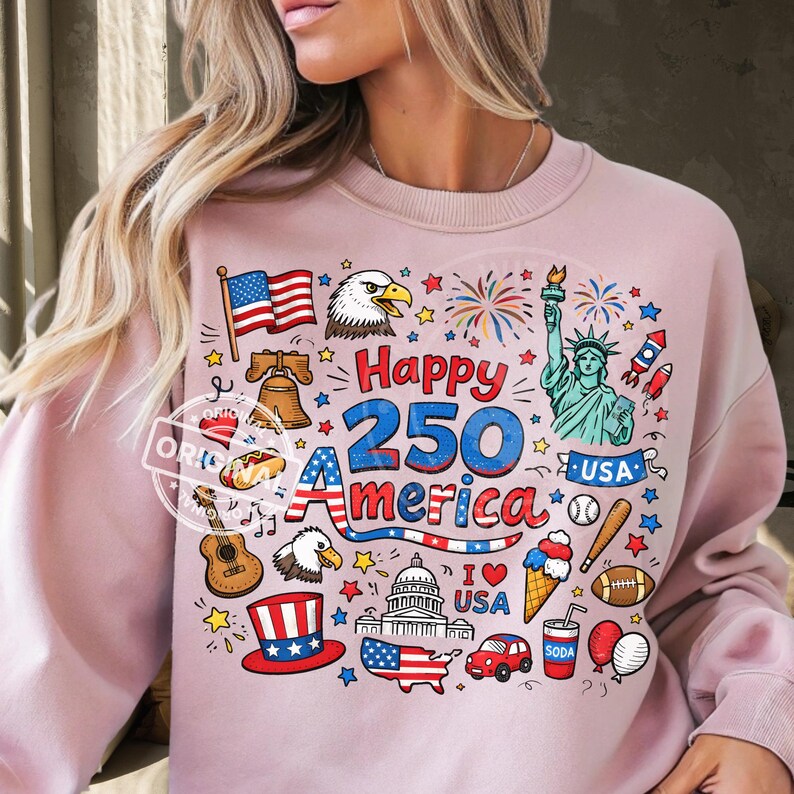 May include: A light pink sweatshirt with a colorful graphic celebrating America's 250th anniversary. The design includes the American flag, an eagle, the Statue of Liberty, fireworks, and other patriotic symbols.