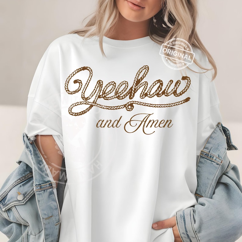 Peut inclure: T-shirt blanc avec l'inscription "Yeehaw and Amen" en lettres marron fa&ccedil;on corde. Le t-shirt a une coupe d&eacute;contract&eacute;e et convient au quotidien. Un petit tampon "ORIGINAL" est visible.