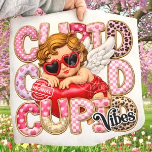 May include: A graphic featuring a cherubic cupid wearing heart-shaped sunglasses, resting on a red heart. The words "Cute Cupid Vibes" are displayed in various pink and gold fonts, with strawberry and leopard print accents. A "Original" stamp is also visible.