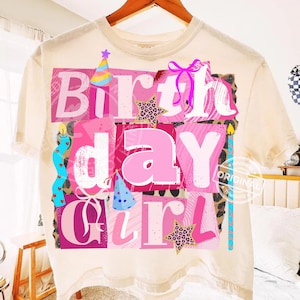 May include: Cream-colored t-shirt with a colorful "Birthday Girl" graphic. The design features pink letters, stars, party hats, and a bow. The graphic has a leopard print background and a blue candle.
