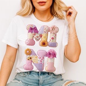 May include: White t-shirt with the letters "M I N I" in a patchwork design. The letters are decorated with floral and gingham patterns, bows, and flower accents. The shirt is worn by a person in blue jeans.