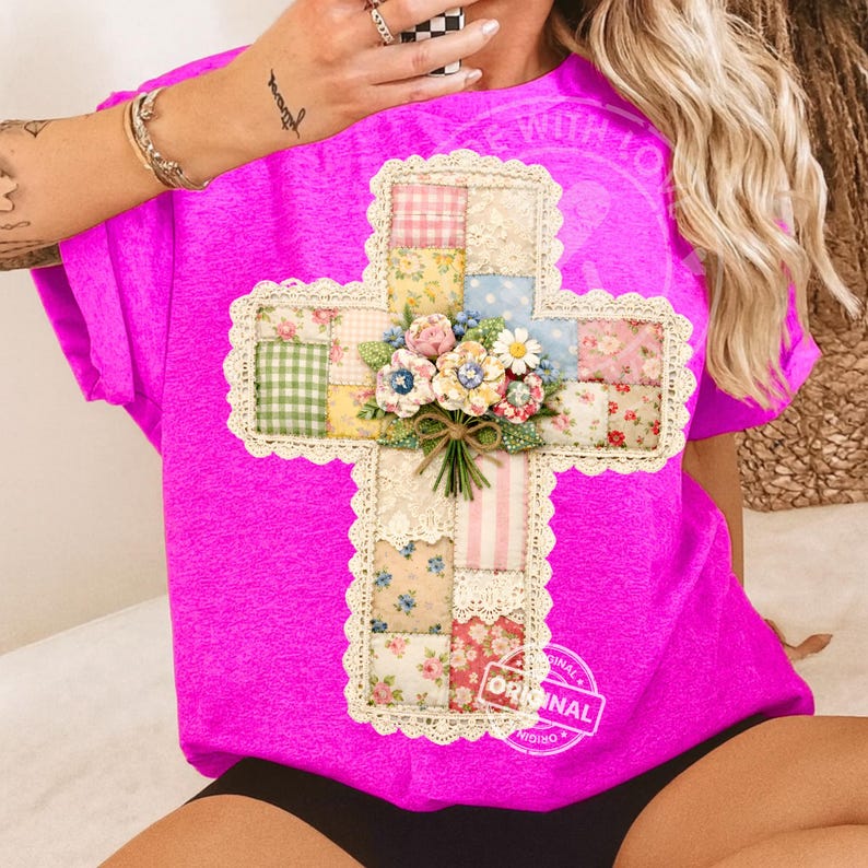 May include: A bright pink t-shirt featuring a cross design. The cross is made of patchwork fabric with floral and patterned squares, lace trim, and a bouquet of flowers at the center. The shirt has the word "ORIGINAL" printed on it.