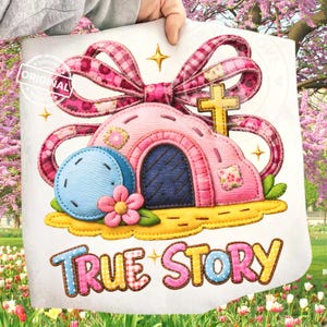 Op de afbeelding: Een stoffen kunstwerk met een roze huis met een blauwe deur, een blauwe bol en een roze bloem. Boven het huis bevinden zich een grote roze strik en een gouden kruis. De woorden "TRUE STORY" zijn in kleurrijke letters gestikt. Het ontwerp staat op een witte achtergrond.