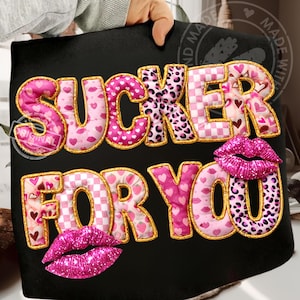 Könnte beinhalten: Schwarze Tragetasche mit dem Schriftzug "SUCKER FOR YOU" in Rosa, Weiß und Leopardenmuster. Das Design umfasst rosa Glitzerlippen. Die Buchstaben sind goldfarben umrandet.