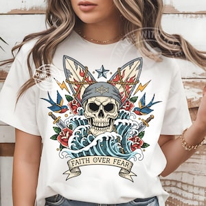 Può includere: T-shirt bianco con un teschio che indossa una bandana e un simbolo a croce, con la scritta "FAITH OVER FEAR". Il design include onde, rose, rondini e fulmini, in stile tatuaggio.