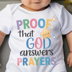 May include: White baby onesie with the text "PROOF that GOD answers PRAYERS" in colorful letters. A smiling star graphic and starbursts are also featured on the onesie. The onesie is short-sleeved.