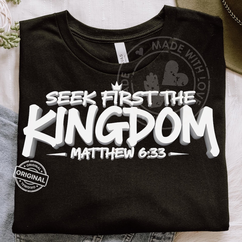 May include: Black t-shirt with the text "SEEK FIRST THE KINGDOM" in white, 3D-style lettering. Below the text is "MATTHEW 6:33". The shirt has a round neckline and a small "ORIGINAL" stamp. A "MADE WITH LOVE" stamp is visible.