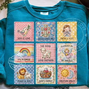 May include: Teal sweatshirt with nine colorful square patches featuring religious themes. Each patch has a different design, including a bird, cross, girl, rainbow, lamb, angel, lion, ark, and sun and moon. Text on the patches includes phrases like "God is Love" and "Jesus Loves Me."