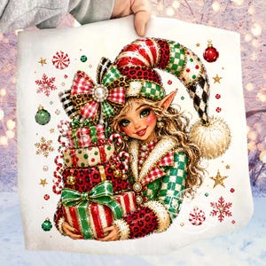 Puede incluir: Un cuadrado de tela blanca con una colorida ilustración de un elfo de pelo largo y ondulado, con un gorro y una chaqueta estampados, que sostiene una pila de cuatro regalos de Navidad envueltos. El diseño incluye detalles festivos en rojo, verde y oro.