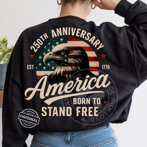 May include: Black sweatshirt featuring a patriotic design. The design includes an eagle, the American flag, and the words "250th Anniversary," "America," and "Born to Stand Free." The year "1776" is also displayed. A circular "Original" logo is visible.