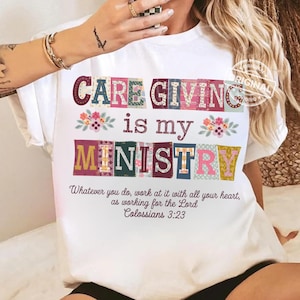 May include: White t-shirt with the text "CARE GIVING is my MINISTRY" in colourful, patterned letters. The shirt also features a Bible verse from Colossians 3:23. Floral accents are placed around the text.