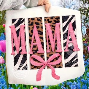 Könnte beinhalten: Ein weißes Stoffquadrat mit dem Wort "MAMA" in rosa, genähten Buchstaben. Die Buchstaben befinden sich über Zebra- und Leopardenmuster-Paneelen. Unten befindet sich eine rosa Schleife. Der Hintergrund ist ein Garten mit rosa und blauen Blumen.