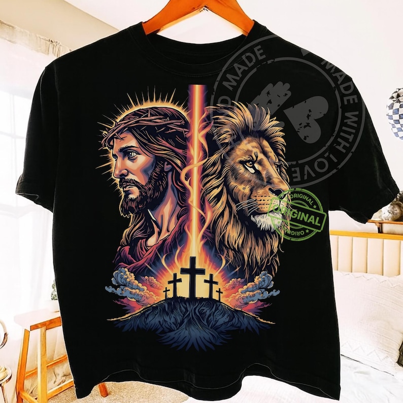 May include: Black t-shirt featuring a graphic design with two portraits: one of Jesus wearing a crown of thorns and the other of a lion. A beam of light connects the two images, with three crosses on a hill below.