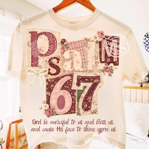 May include: Cream-colored t-shirt with the text "Psalm 67" in a patchwork design. The design includes floral patterns, the number 67, and the quote "God be merciful to us and bless us, and cause His face to shine upon us."