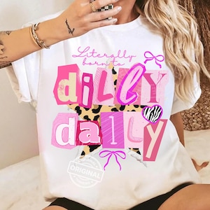 Puede incluir: Camiseta blanca con la frase "Literally born to dilly dally" en rosa, con un diseño de estrella y corazón. El diseño incorpora varios tonos de rosa, un corazón con estampado de cebra y un fondo de estampado de leopardo.