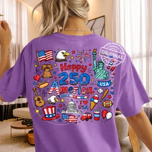 May include: A purple t-shirt with a graphic design celebrating the 250th anniversary of America. The design includes the American flag, Statue of Liberty, fireworks, and the text "Happy 250 America".