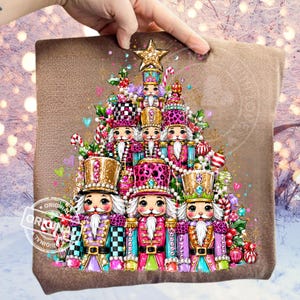 Può includere: Una felpa marrone con una stampa grafica di un albero di Natale composto da diverse figure di schiaccianoci. Gli schiaccianoci sono decorati nei toni del rosa, oro e verde acqua con motivi leopardati e a scacchi, sormontati da una stella dorata.